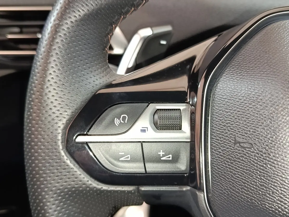 Gros plan sur les commandes gauche du volant cuir perforé du Peugeot 5008 GT 2023, boutons multifonctions noirs.