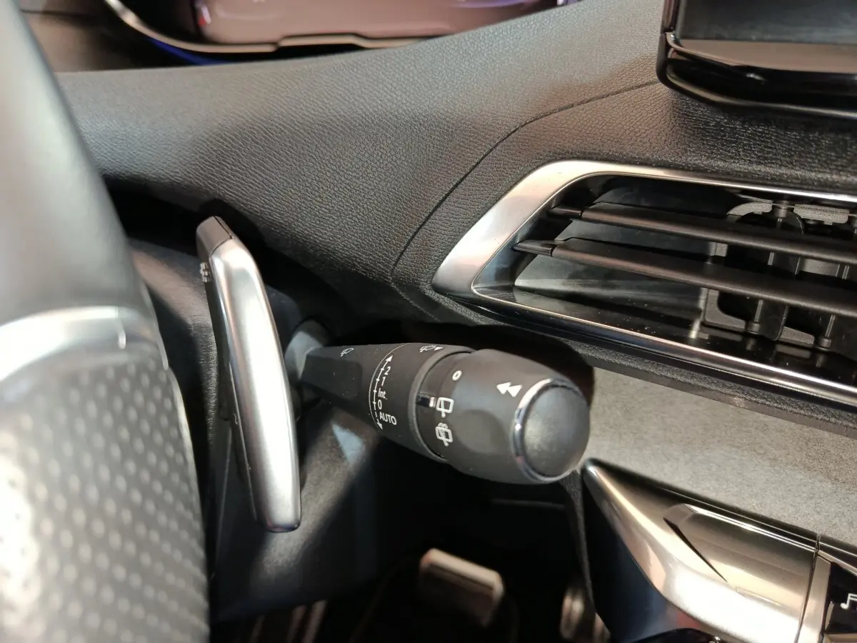 Gros plan sur la commande d’essuie-glace à gauche du volant dans l’habitacle noir du Peugeot 5008 bleu.