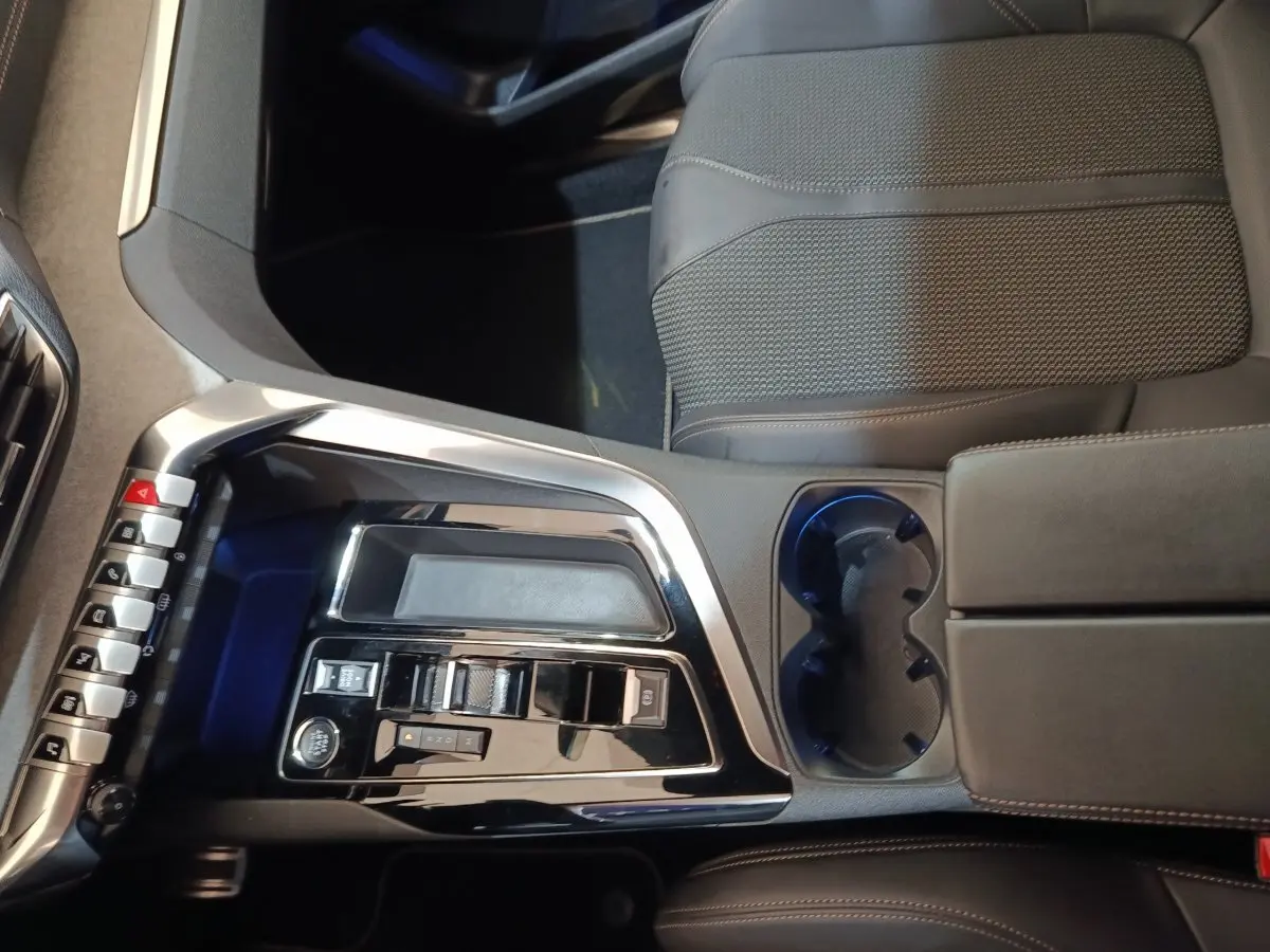 Vue intérieure centrée sur la console centrale noire brillante et les sièges en tissu gris du Peugeot 5008 GT 2023.