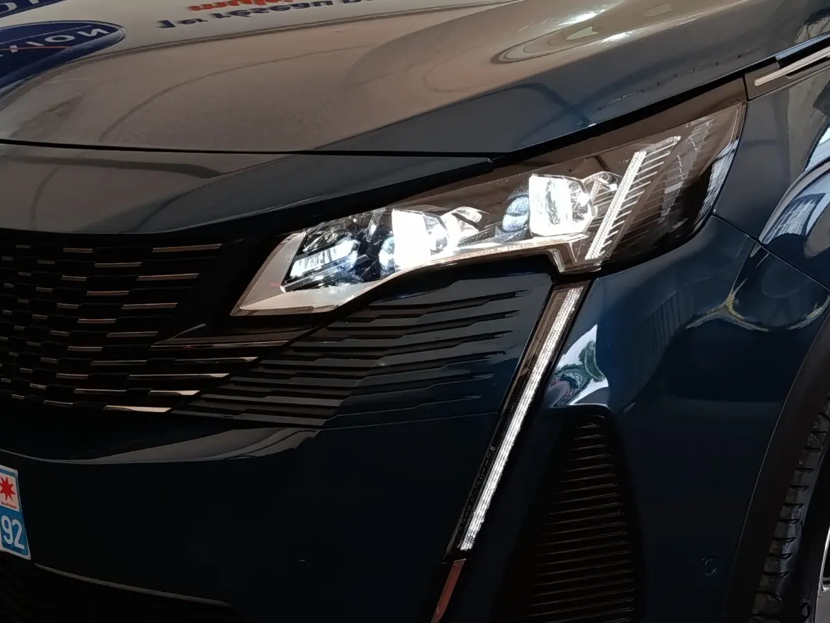 Gros plan sur l'avant droit bleu du Peugeot 5008 2023, mettant en valeur le phare LED et la calandre noire.