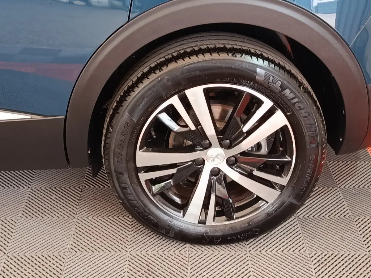 Gros plan sur la roue arrière droite d’un Peugeot 5008 bleu 2023, jante alliage bicolore et pneu Michelin.