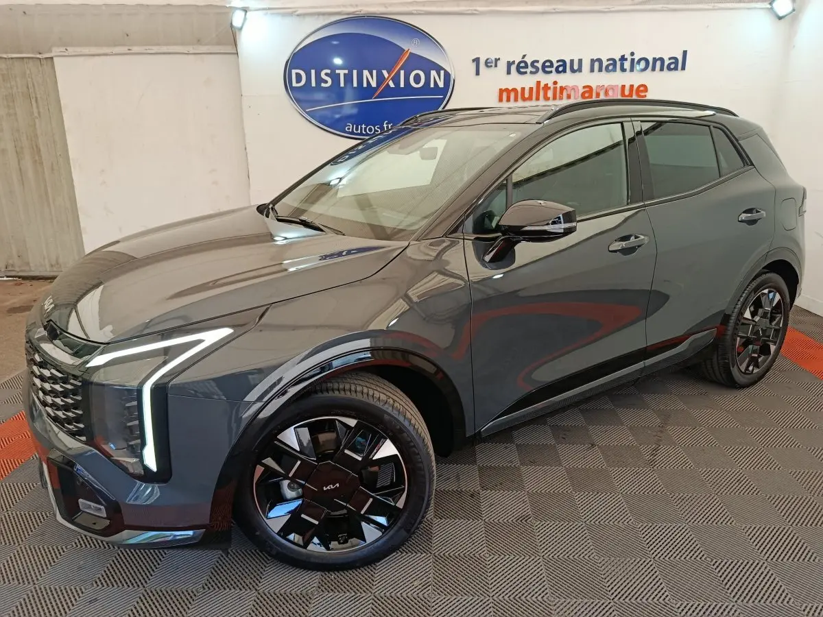 KIA Sportage 2026 gris foncé en 3/4 avant droit, avec phares LED verticaux et jantes noires distinctives.