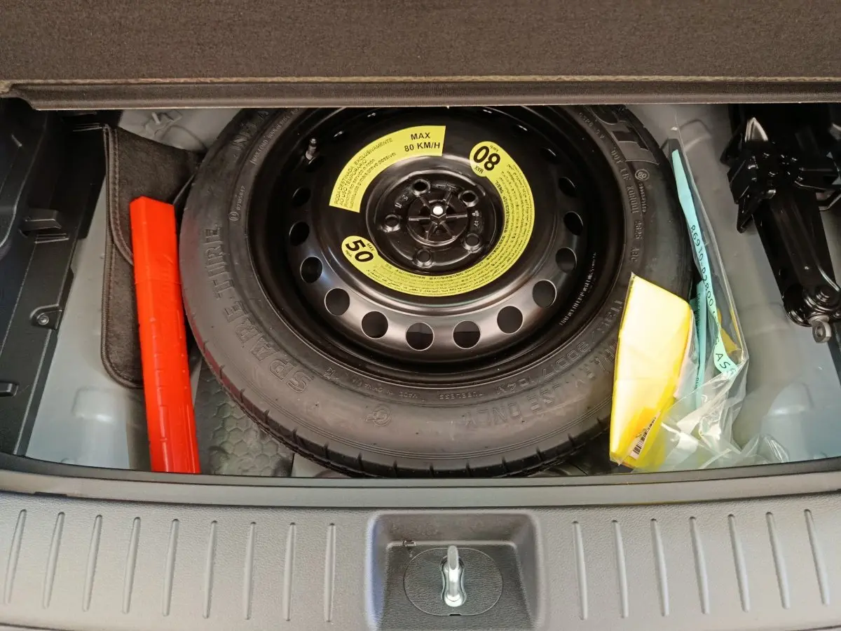 Vue plongeante sur la roue de secours noire et ses accessoires dans le coffre d’un Kia Sportage gris foncé.