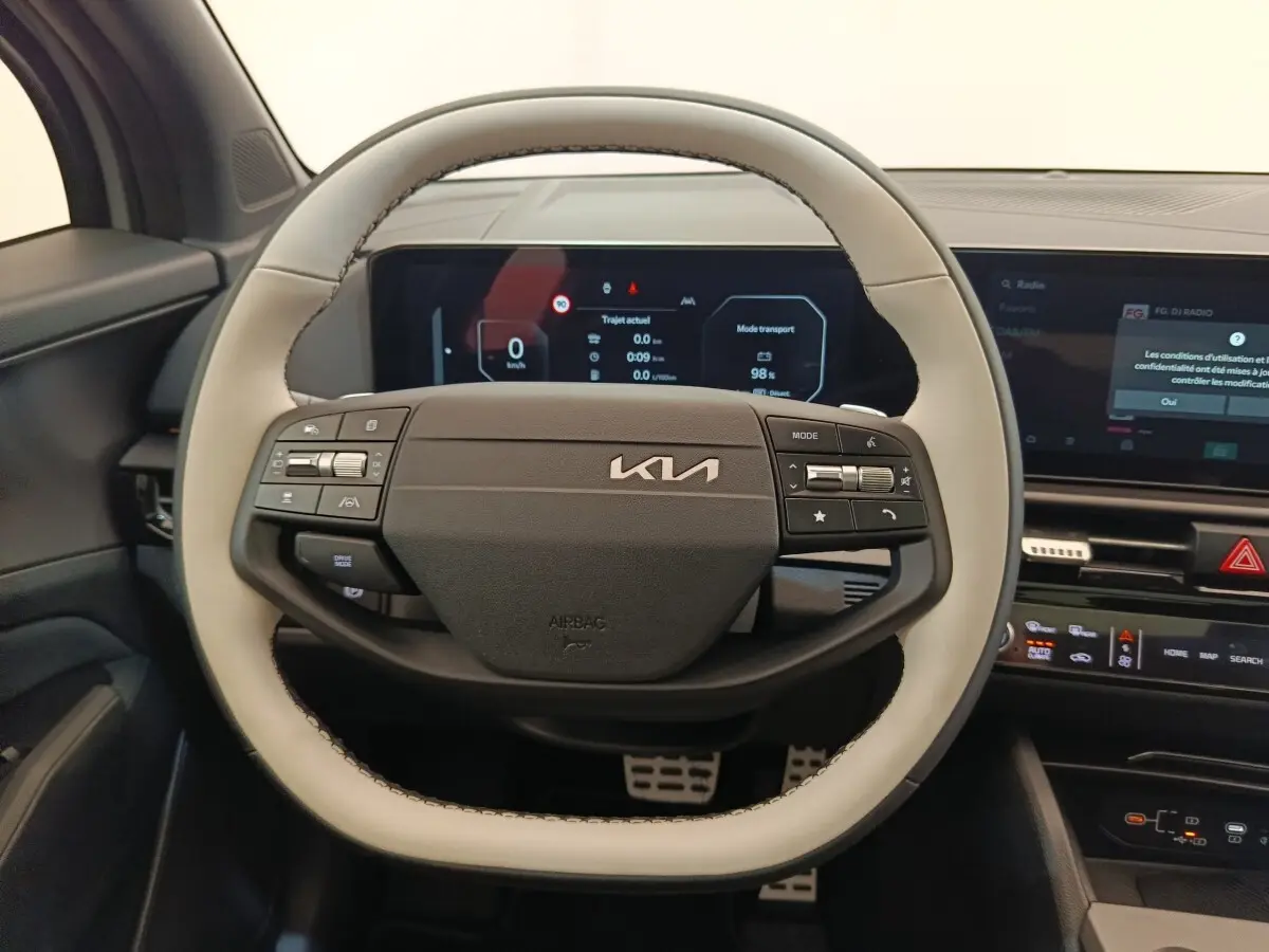 Vue rapprochée du volant bicolore gris clair et noir du Kia Sportage 2026 avec tableau de bord numérique en arrière-plan.