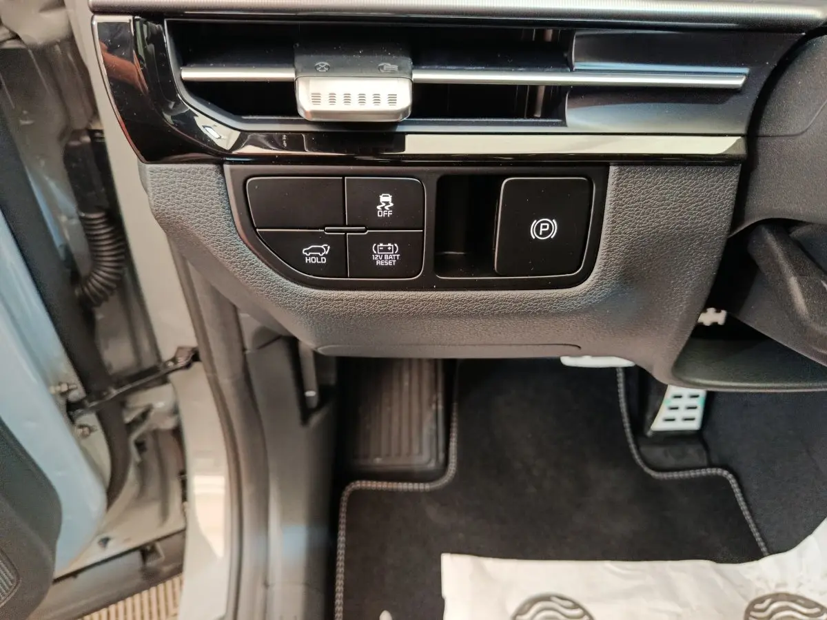 Détail des commandes sous le tableau de bord côté gauche du Kia Sportage gris foncé 2026, avec bouton frein à main électrique.