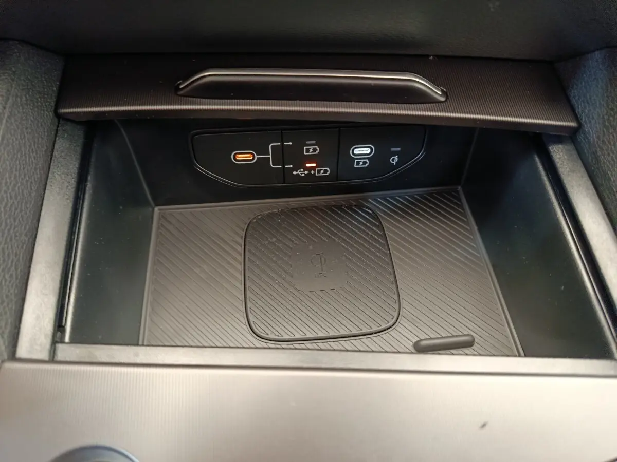 Vue rapprochée de la zone de recharge sans fil et ports USB du coffre central noir du Kia Sportage gris foncé 2026.