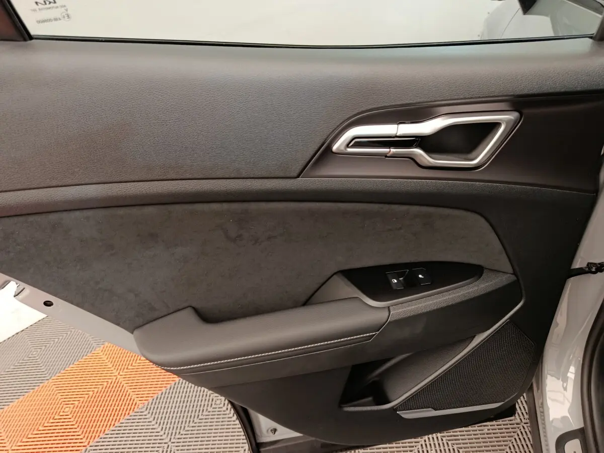 Vue intérieure côté gauche de la porte avant d’un KIA SPORTAGE gris foncé avec garniture noire et commandes de vitres.