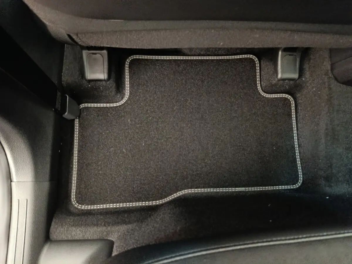 Tapis de sol noir avec surpiqûres blanches côté conducteur d'un KIA Sportage gris foncé, vue intérieure au sol.
