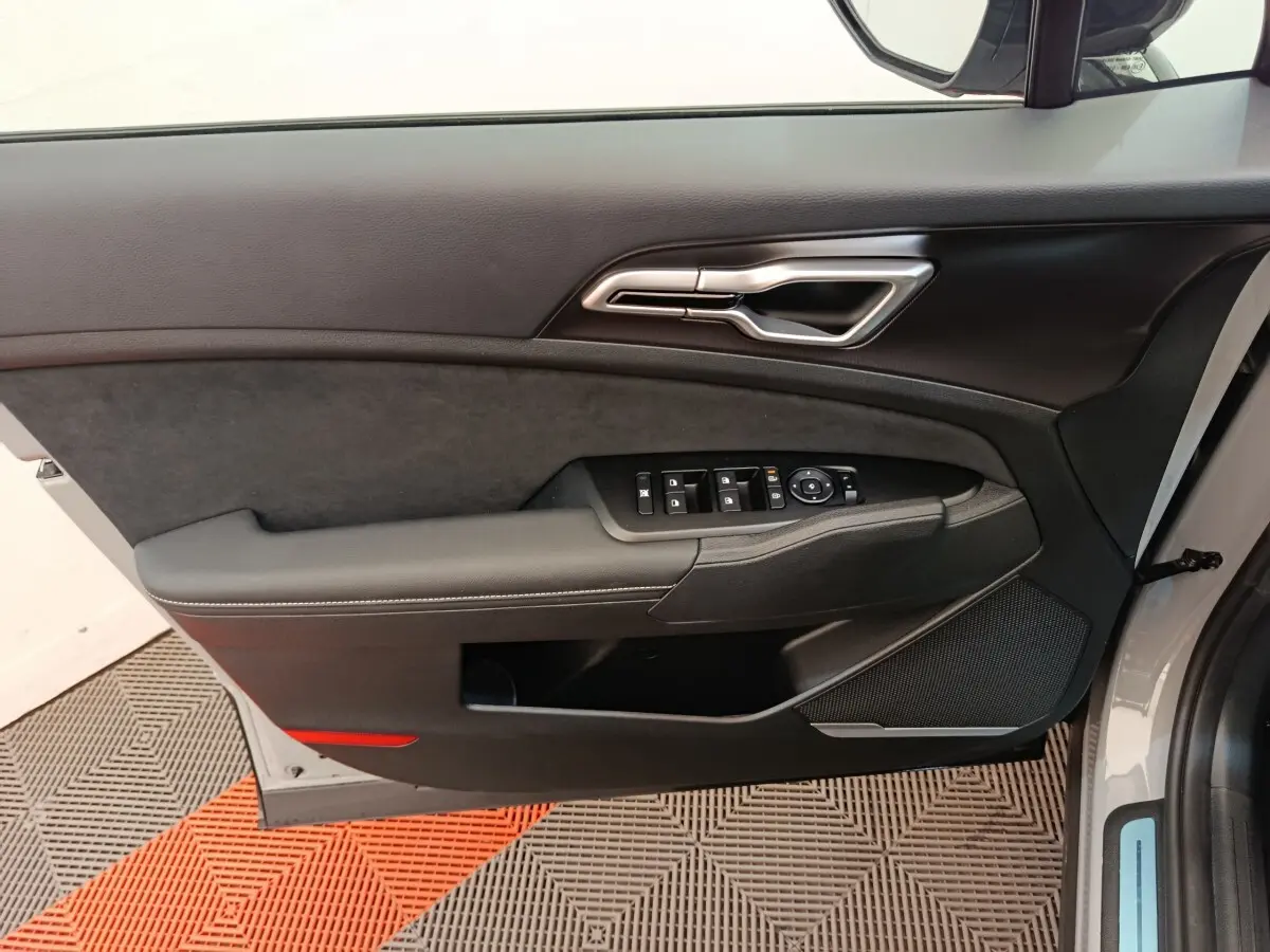 Vue intérieure côté gauche de la porte avant gris foncé du Kia Sportage 2026 avec commandes de vitres et poignée argentée.