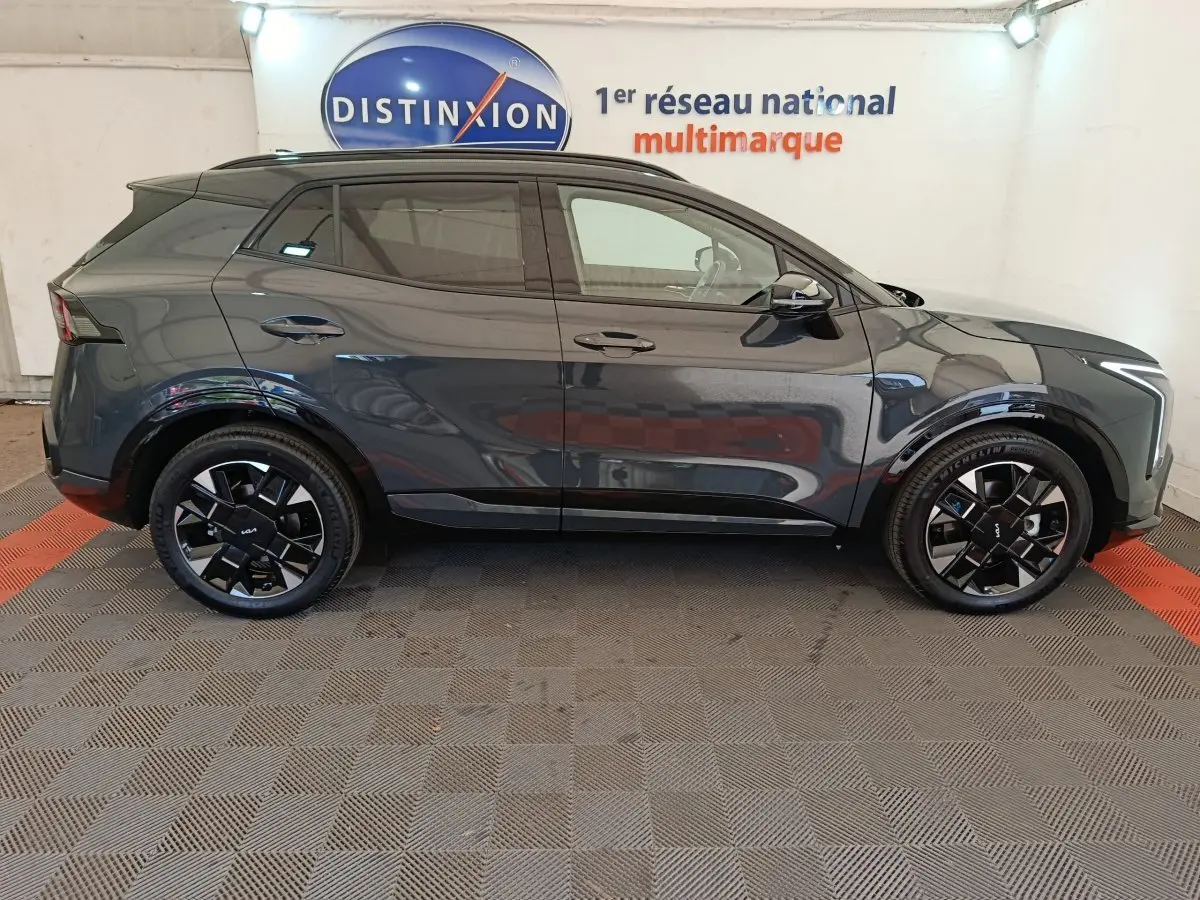 Vue latérale droite du KIA SPORTAGE gris foncé 2026 avec jantes noires et toit noir en showroom.