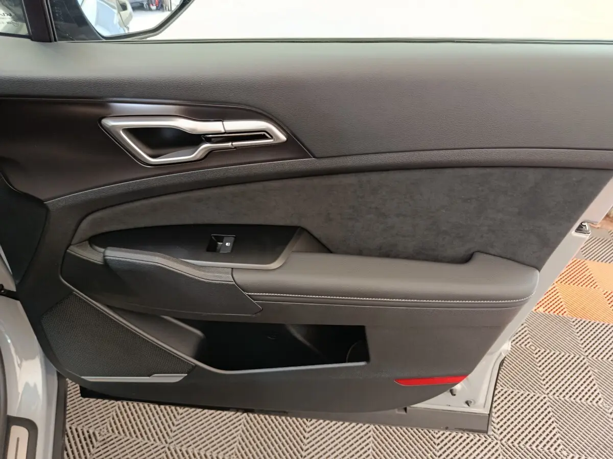 Vue intérieure côté gauche de la porte avant gris foncé du Kia Sportage avec poignée argentée et accoudoir rembourré.