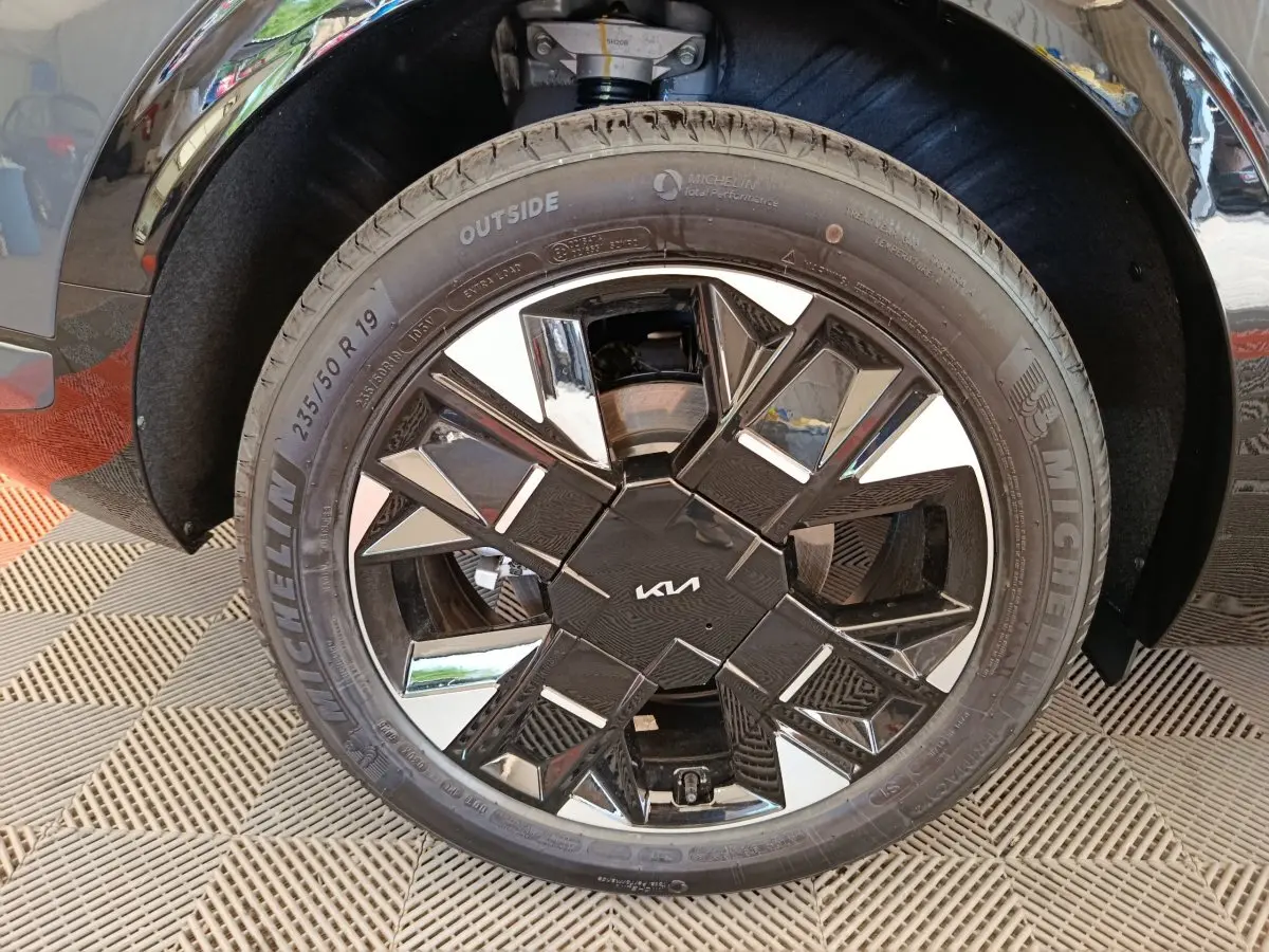Gros plan sur la roue avant droite du KIA SPORTAGE gris foncé, mettant en valeur la jante noire et chromée au design géométrique.