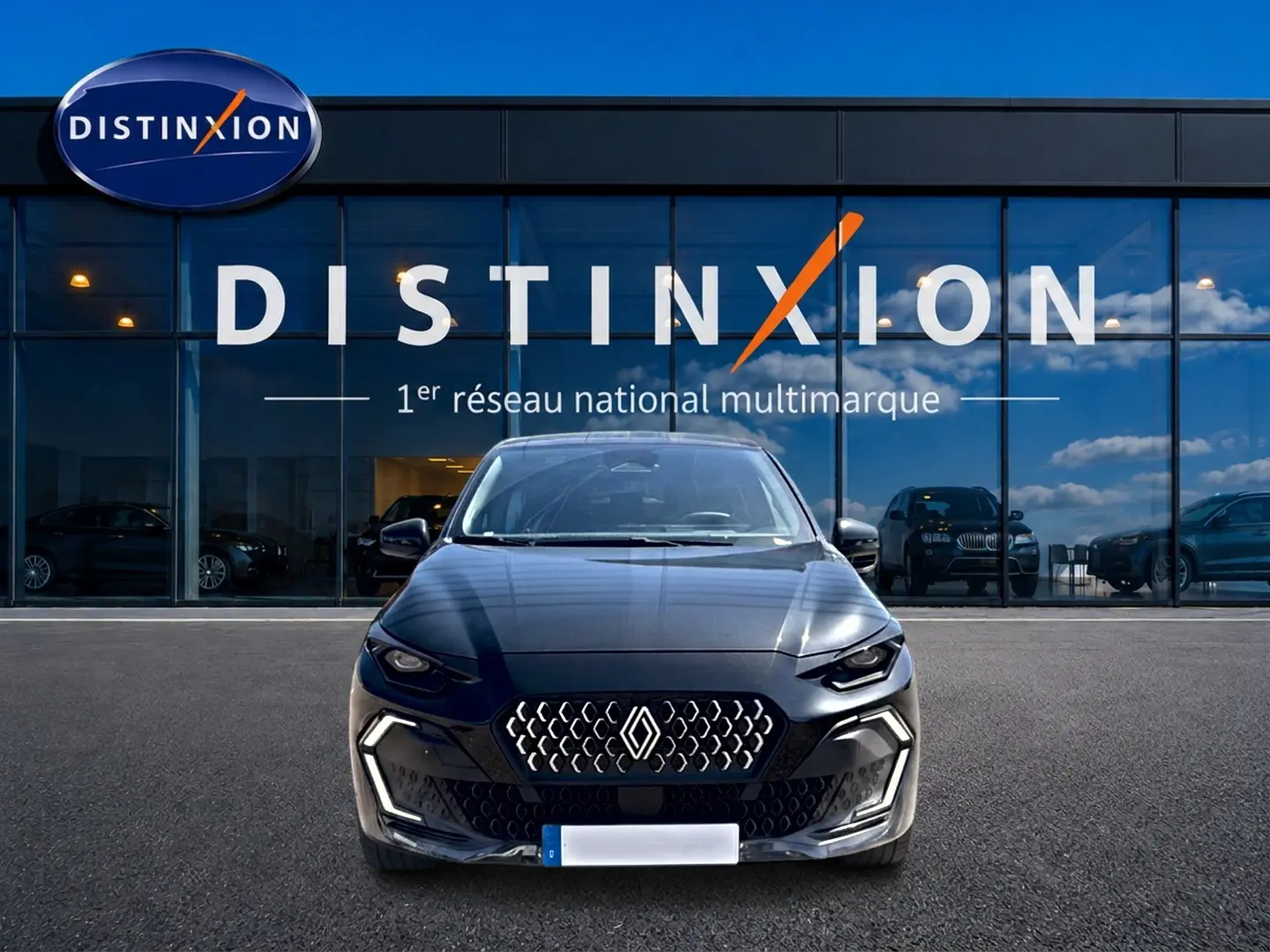 Vue frontale d'une Renault Clio VI noire garée devant une vitrine avec logo Distinxion en arrière-plan.