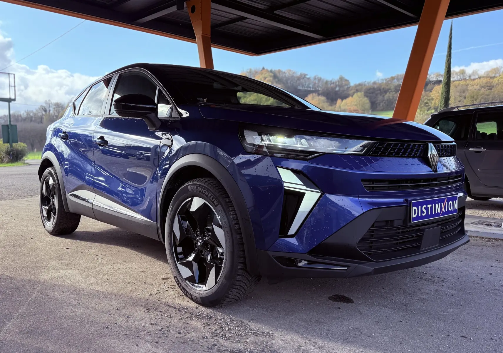 Renault Captur E-Tech hybride 2025 bleu Iron Metal avec toit noir, vue 3/4 avant droit sous abri.