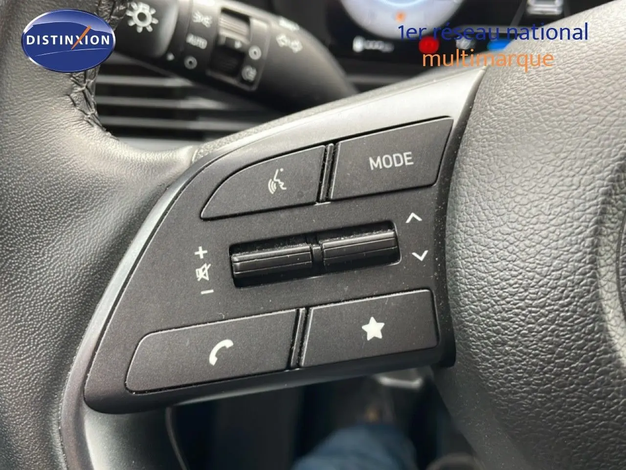 Gros plan sur les commandes au volant côté gauche d'une Hyundai i20 noire Phantom Metal 2025, boutons multifonctions visibles.