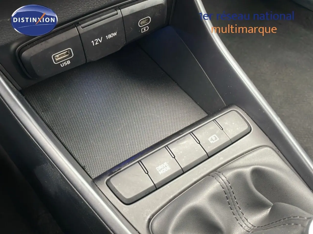 Gros plan sur la console centrale noire de la Hyundai i20 2025, montrant les ports USB, prise 12V et boutons de commande près du levier de vitesses.