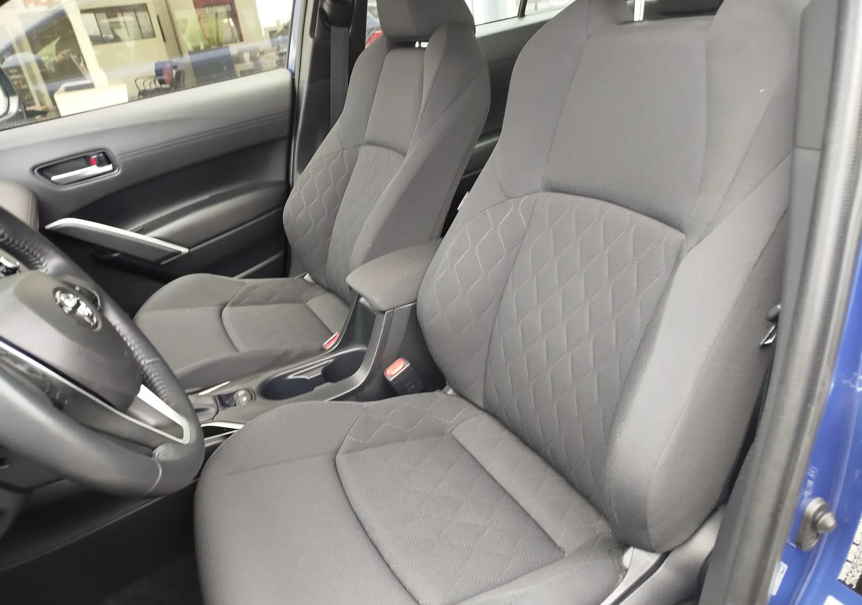 Vue intérieure côté conducteur de la Toyota Corolla Cross 1.8l 140h Dynamic bleu cosmique, sièges tissu gris avec motifs losanges.