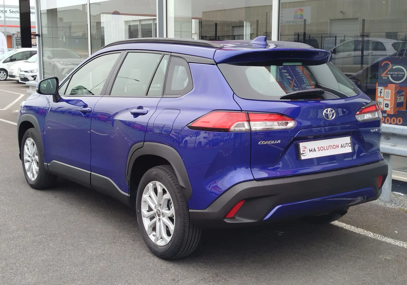 Vue 3/4 arrière droite d’un Toyota Corolla Cross bleu cosmique avec toit noir et jantes alliage argentées.