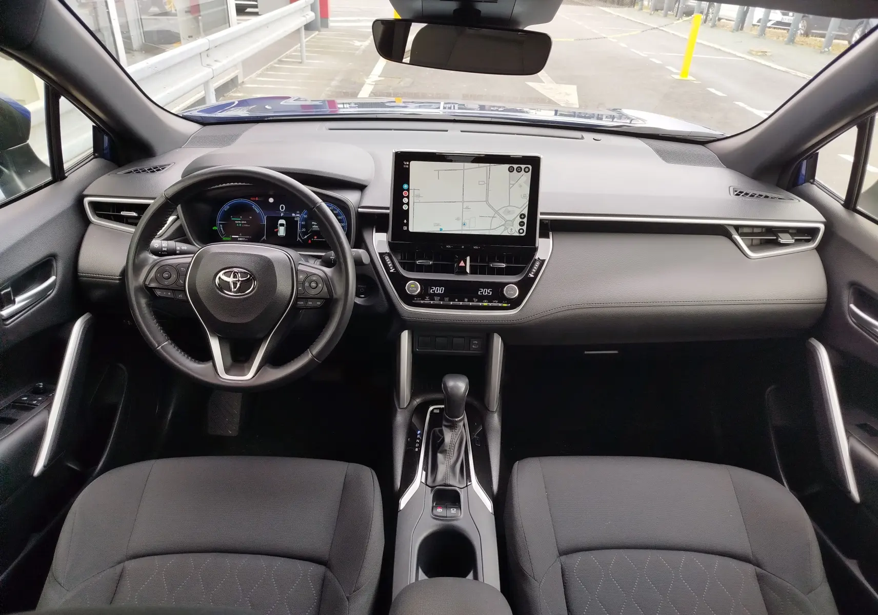 Vue intérieure avant de la Toyota Corolla Cross 1.8l 140h Dynamic 2024, tableau de bord gris avec écran tactile central et volant multifonction.