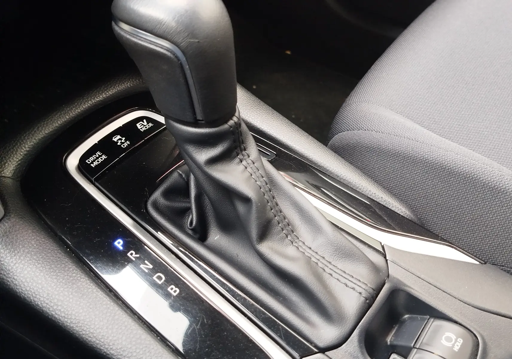 Le levier de vitesses automatique noir du Toyota Corolla Cross 1.8l 140h Dynamic, vu en gros plan côté conducteur.