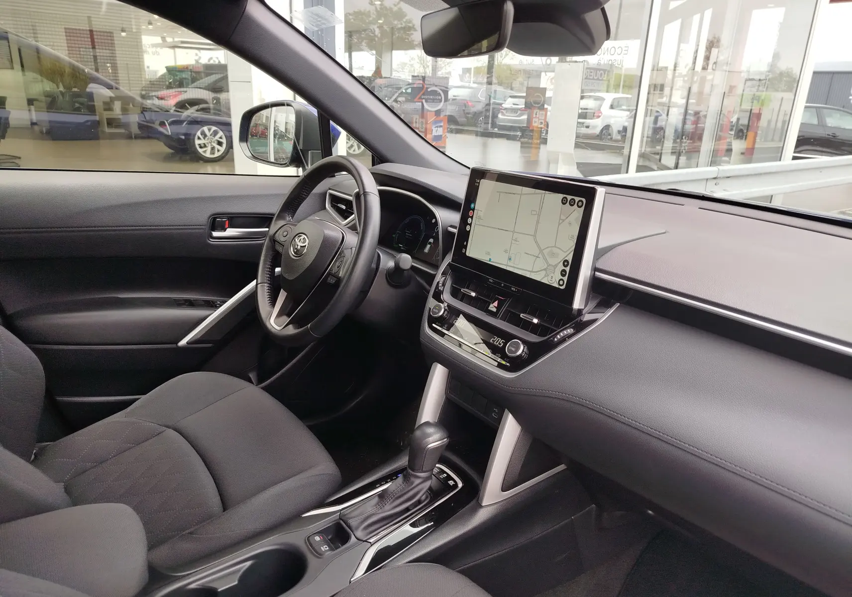 Intérieur de la Toyota Corolla Cross 2024 vue côté conducteur, tableau de bord noir avec écran tactile et boîte auto.