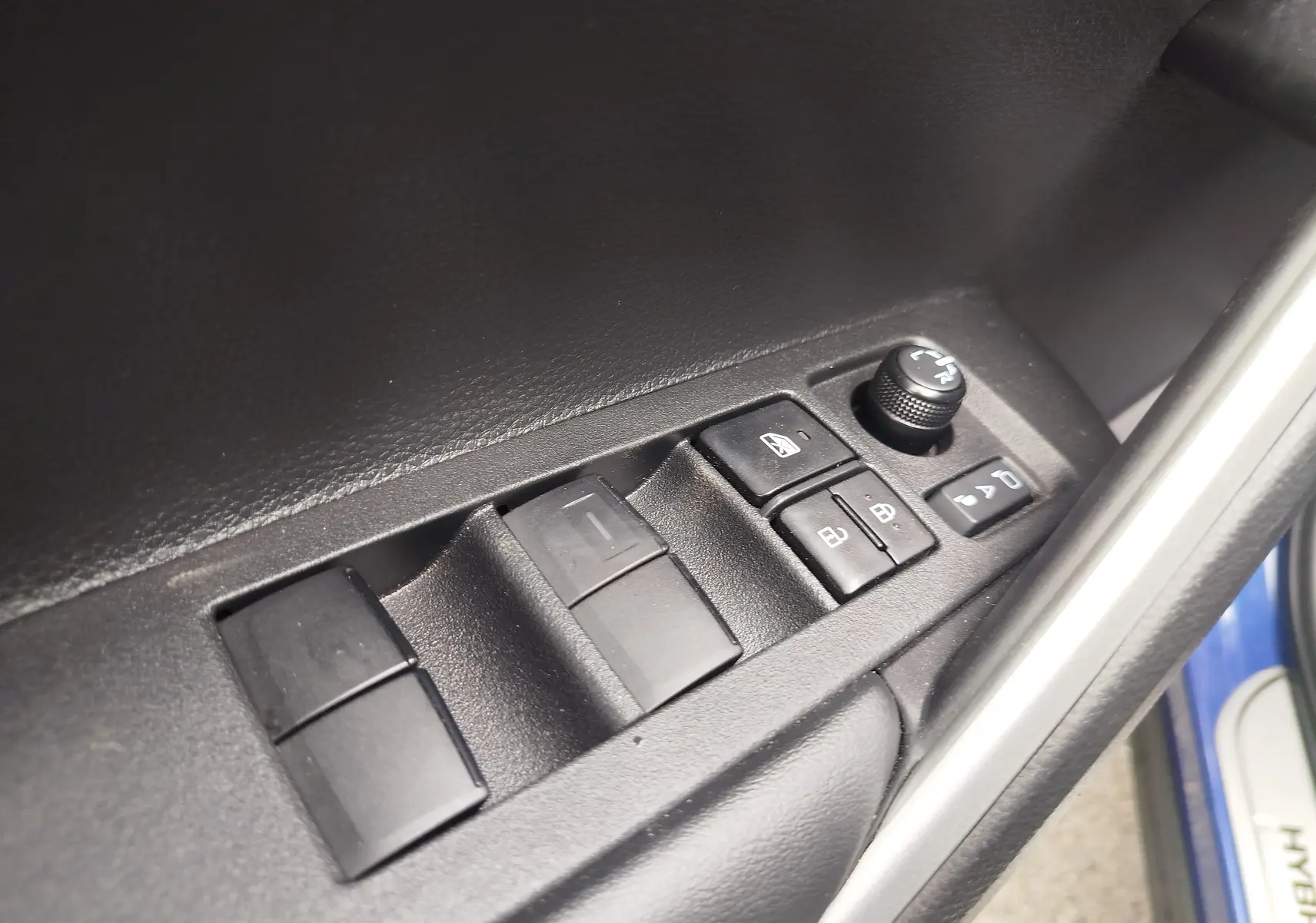 Gros plan sur les commandes de lève-vitres et rétroviseurs côté conducteur, intérieur noir du Toyota Corolla Cross bleu cosmique 2024.