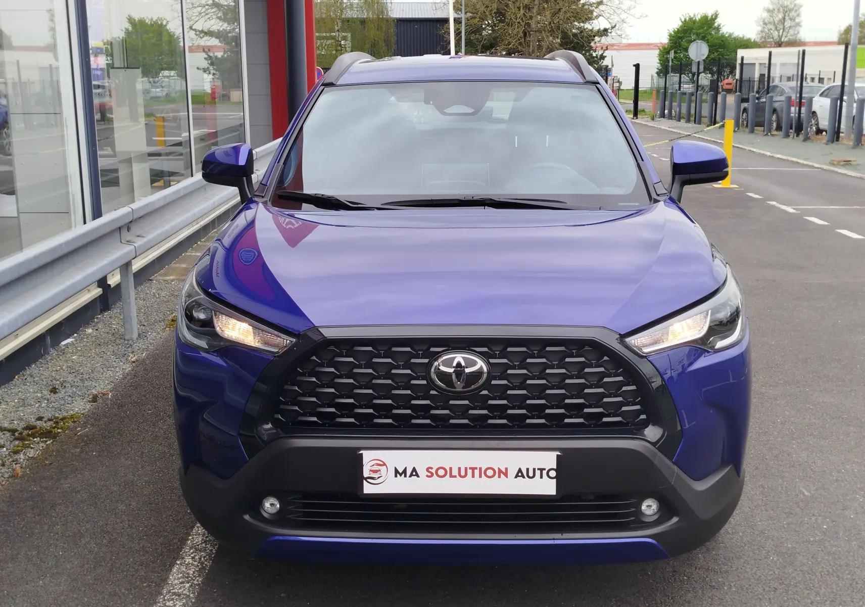 Vue avant frontale du Toyota Corolla Cross 1.8l 140h Dynamic en bleu cosmique avec calandre noire et feux allumés.