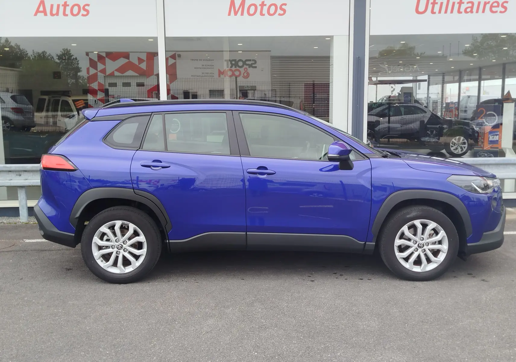 Profil latéral droit d'un Toyota Corolla Cross 1.8l 140h Dynamic bleu cosmique, avec jantes alliage et protections noires sur les bas de caisse.