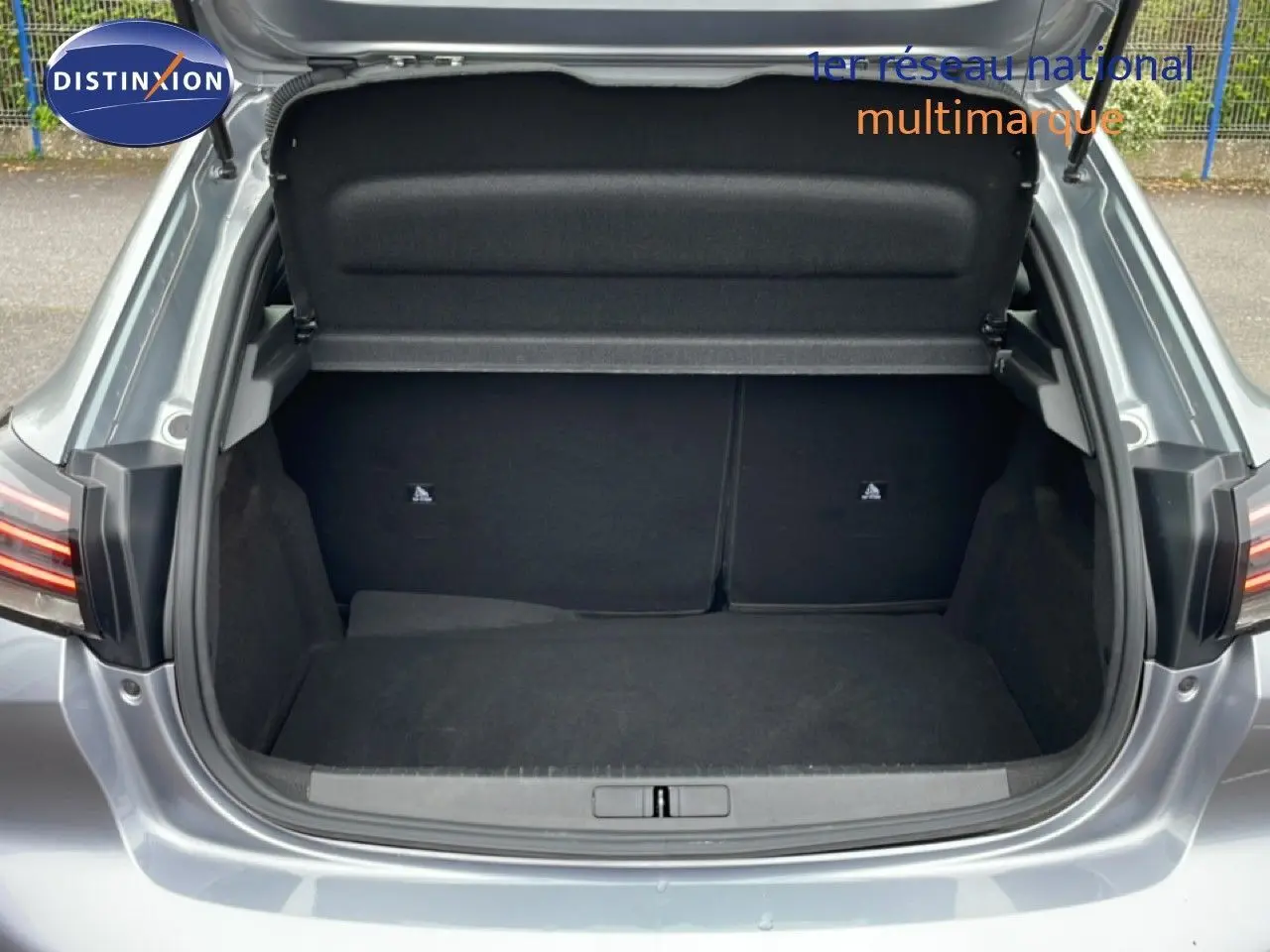 Coffre ouvert vu de l'arrière d'une Peugeot 208 gris Artense métal, montrant l'espace de chargement vide.