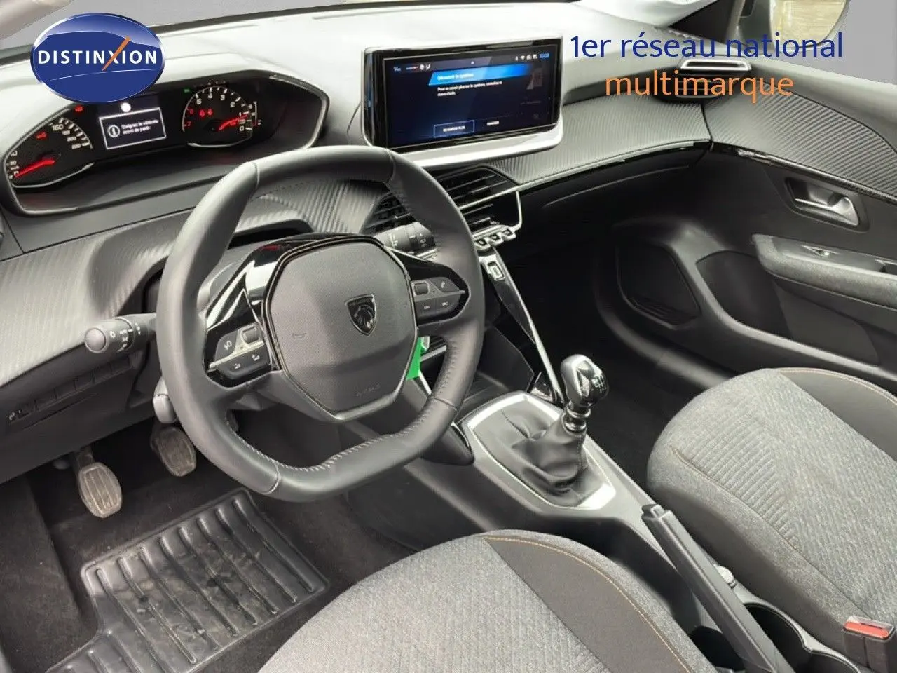 Intérieur de Peugeot 208 2025 vu côté conducteur, volant cuir multifonction, console centrale avec boîte manuelle et écran tactile.