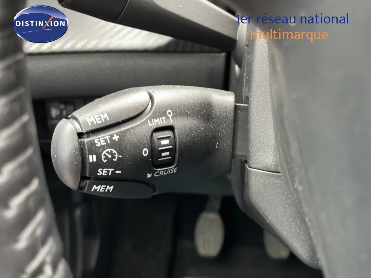 Gros plan sur la commande de régulateur de vitesse à gauche du volant dans l’habitacle d’une Peugeot 208 gris Artense.