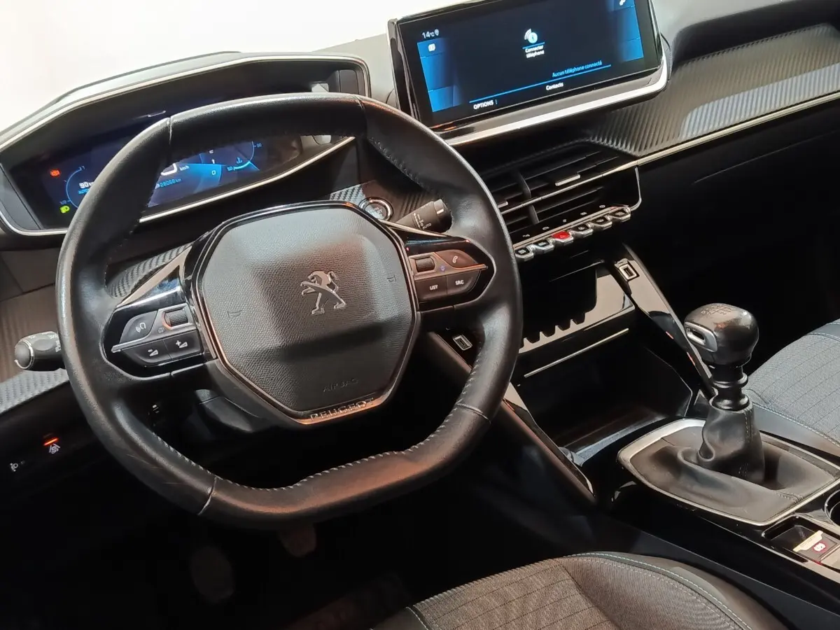 Vue intérieure centrée sur le volant cuir et la console centrale avec levier de vitesse manuelle de la Peugeot 208 blanche.