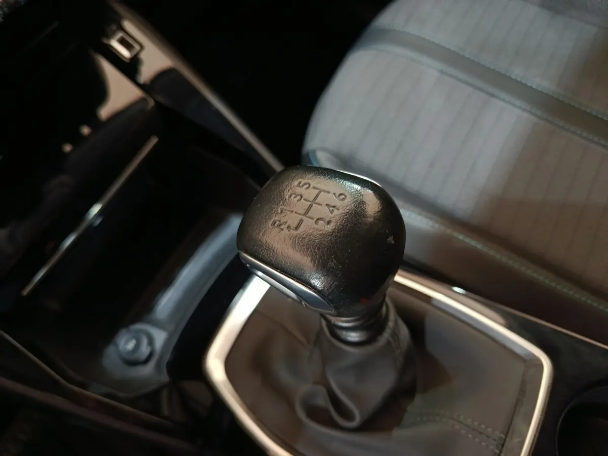 Gros plan sur le levier de vitesses manuel noir et la sellerie grise à motifs de la Peugeot 208 PureTech 100 S&S Allure Business.