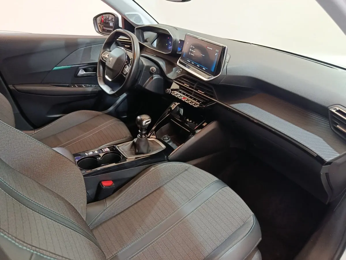 Vue intérieure côté conducteur de la Peugeot 208 blanche, montrant le tableau de bord et la console centrale avec écran tactile.