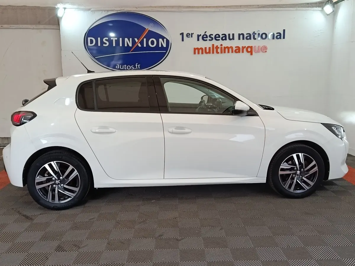 Vue de profil côté gauche d'une Peugeot 208 blanche PureTech 100 S&S Allure Business avec jantes alliage et vitres teintées.