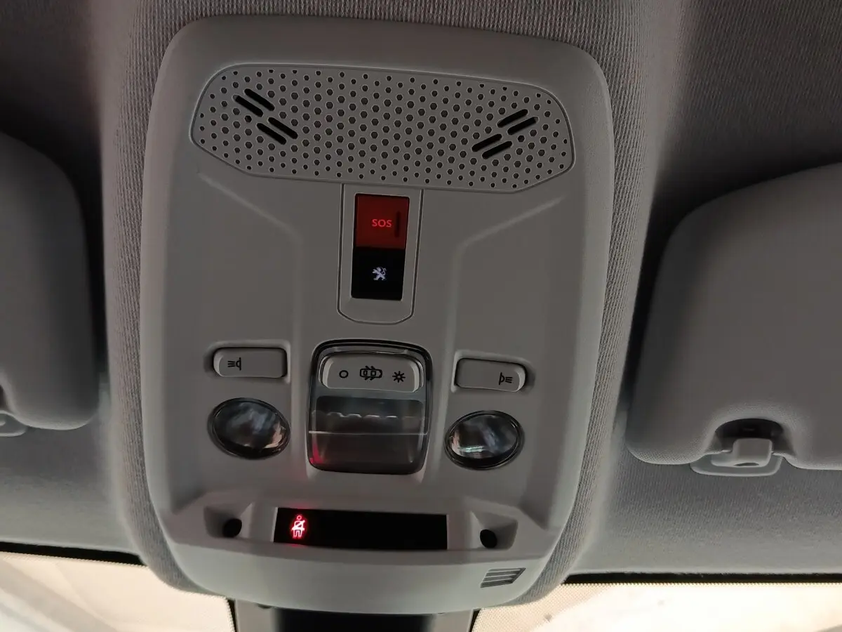Vue en contre-plongée du panneau de commandes au plafond intérieur du Peugeot 208 blanc, avec bouton SOS rouge et éclairages intégrés.