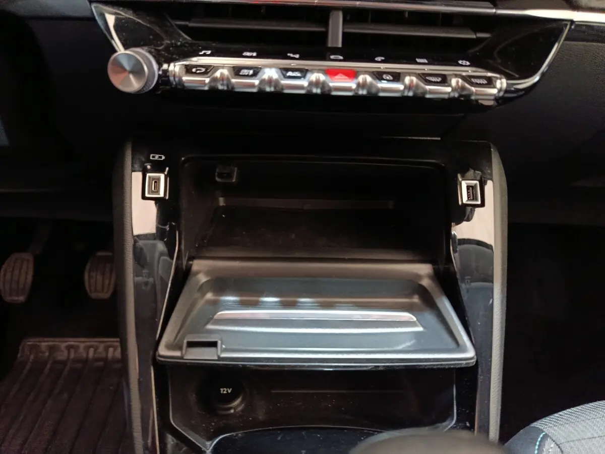 Vue rapprochée de la console centrale noire du Peugeot 208 blanc, avec ports USB et commandes en rangée chromée.
