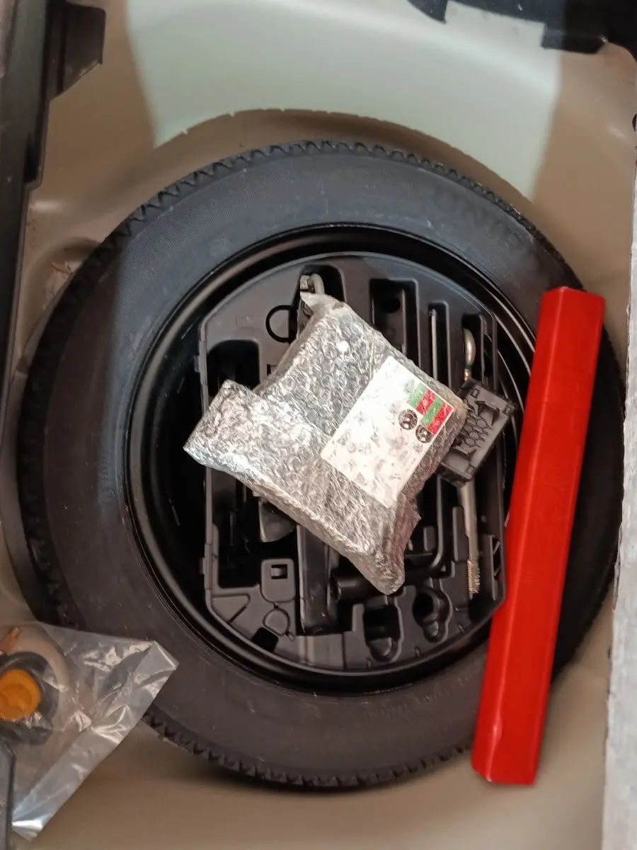 Vue plongeante sur la roue de secours noire et les outils de bord dans le coffre d’une Peugeot 208 blanche.