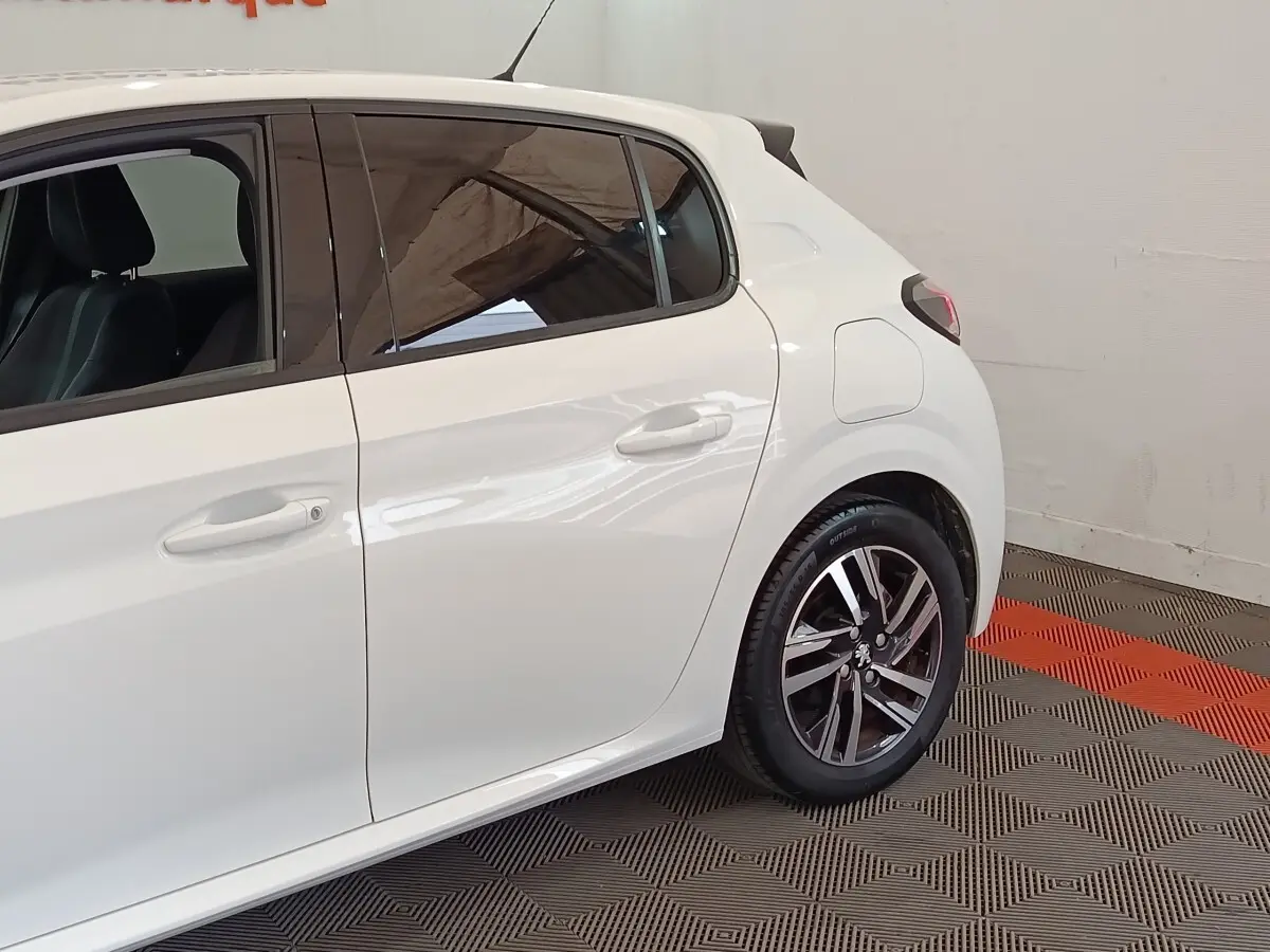 Vue latérale droite sur l’arrière d’une Peugeot 208 blanche avec jantes alliage et vitres teintées.