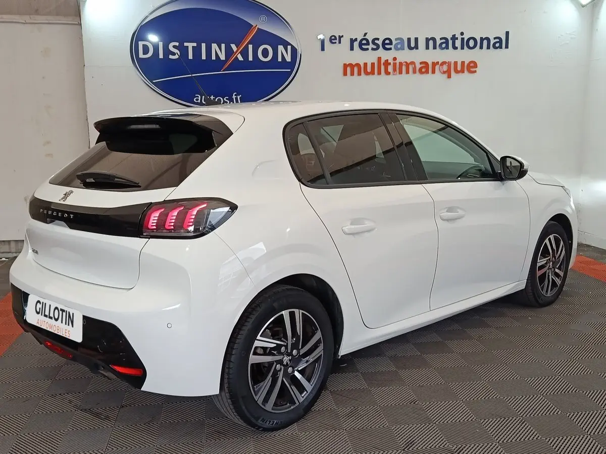 Vue 3/4 arrière droite d'une Peugeot 208 blanche avec feux arrière LED et jantes alliage bicolores.