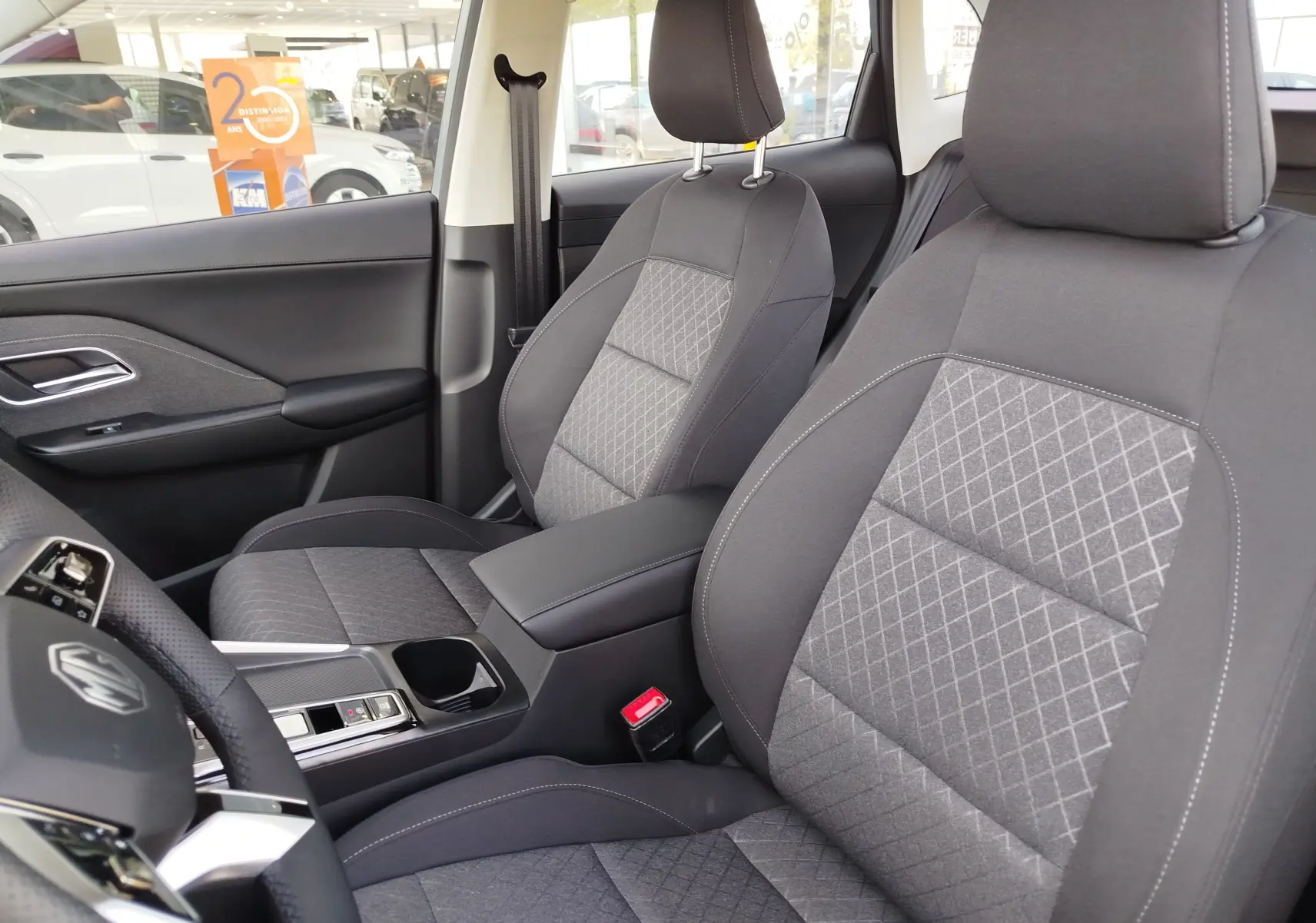 Vue intérieure sur les sièges avant gris à motifs du MG ZS 1.5 L Hybrid+ 2026, avec console centrale et volant partiel visible.