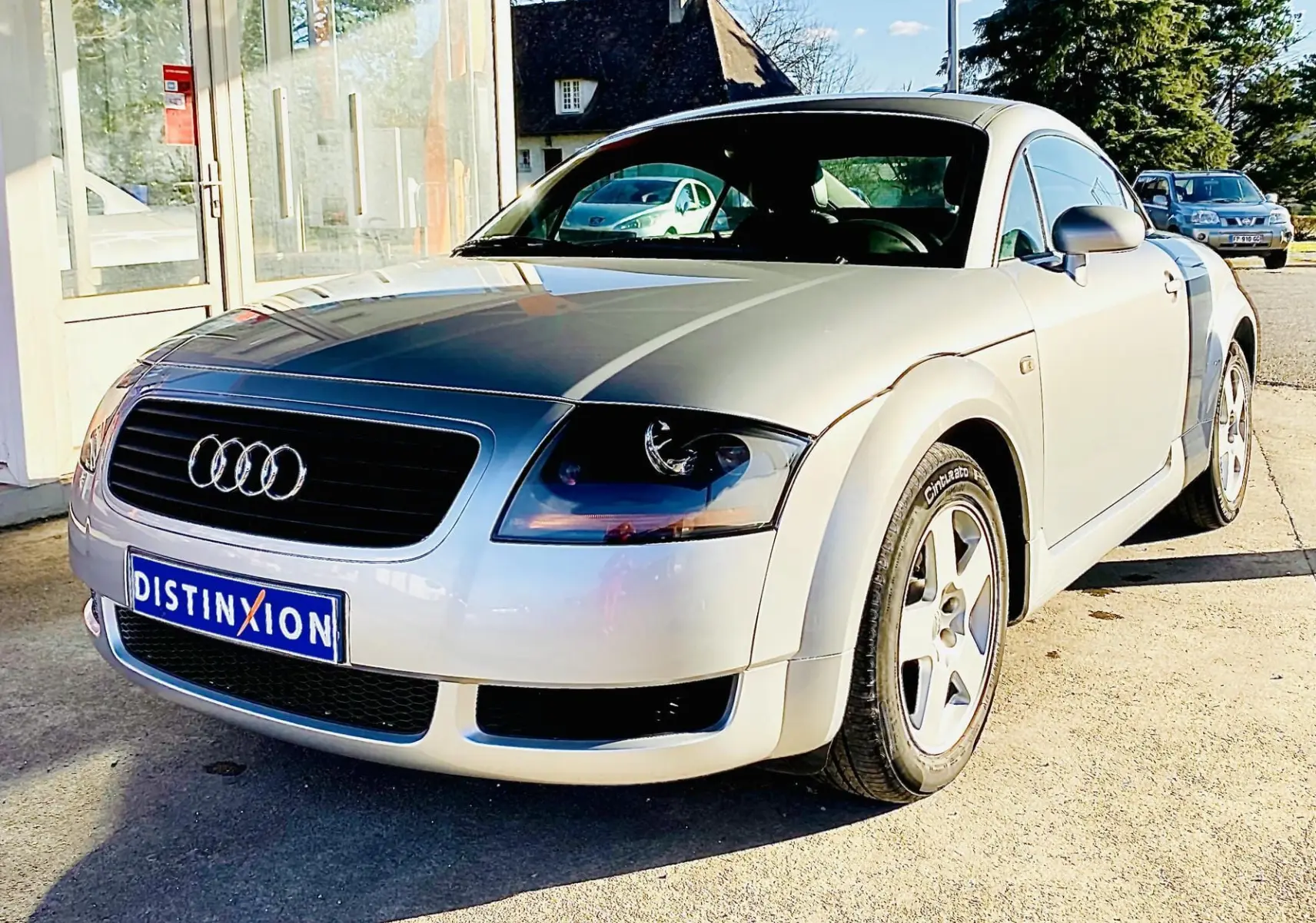 Audi TT Coupé gris vue 3/4 avant droit, avec calandre noire et jantes alliage cinq branches.