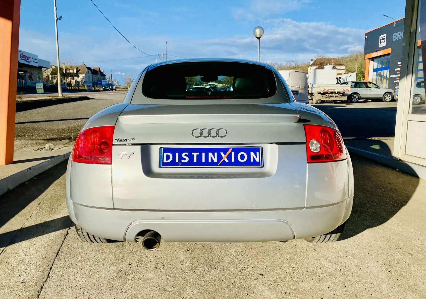 Vue arrière d'une Audi TT Coupé gris clair de 2002 avec feu arrière rouge et plaque d'immatriculation bleue Distinxion.