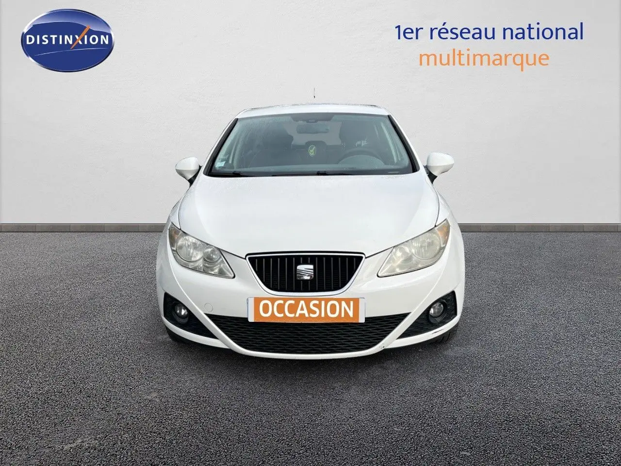 Vue de face d'une SEAT Ibiza blanche 1.6 TDI 90CH STYLE de 2010 avec plaque "OCCASION" sur un sol gris.