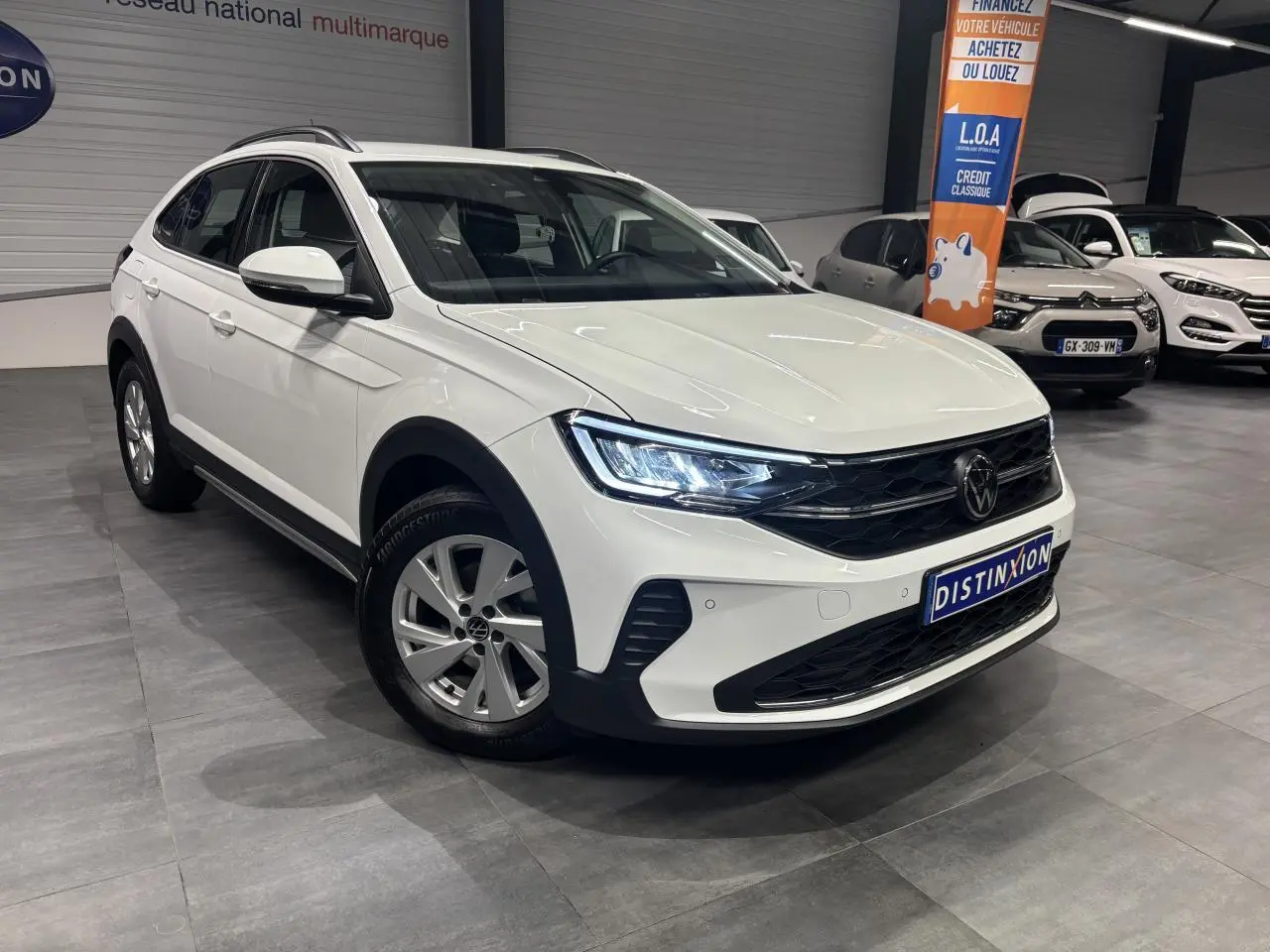 Volkswagen Taigo blanc en 3/4 avant droit, avec jantes alliage et calandre noire brillante en showroom.