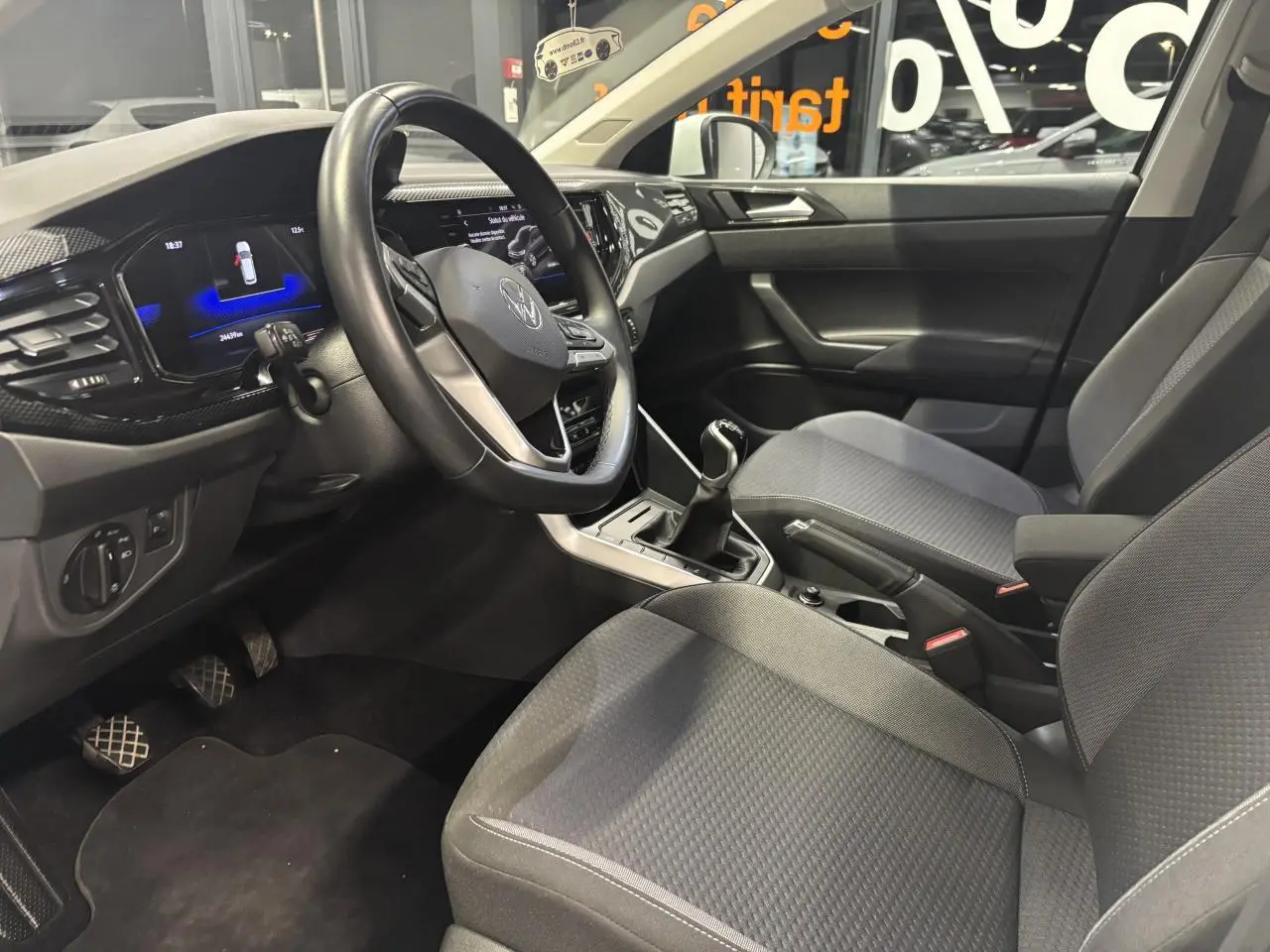 Vue intérieure côté conducteur du Volkswagen Taigo 1.0 TSI 2023, montrant le volant cuir multifonctions et la sellerie tissu grise.