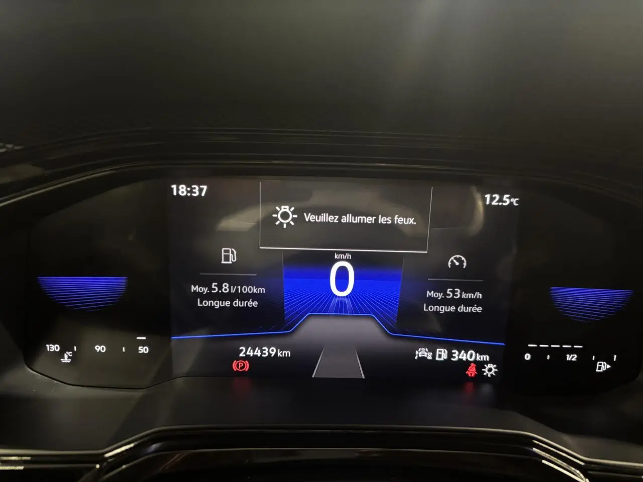 Tableau de bord numérique du Volkswagen Taigo 2023 affichant vitesse, consommation et alertes, vue frontale rapprochée.