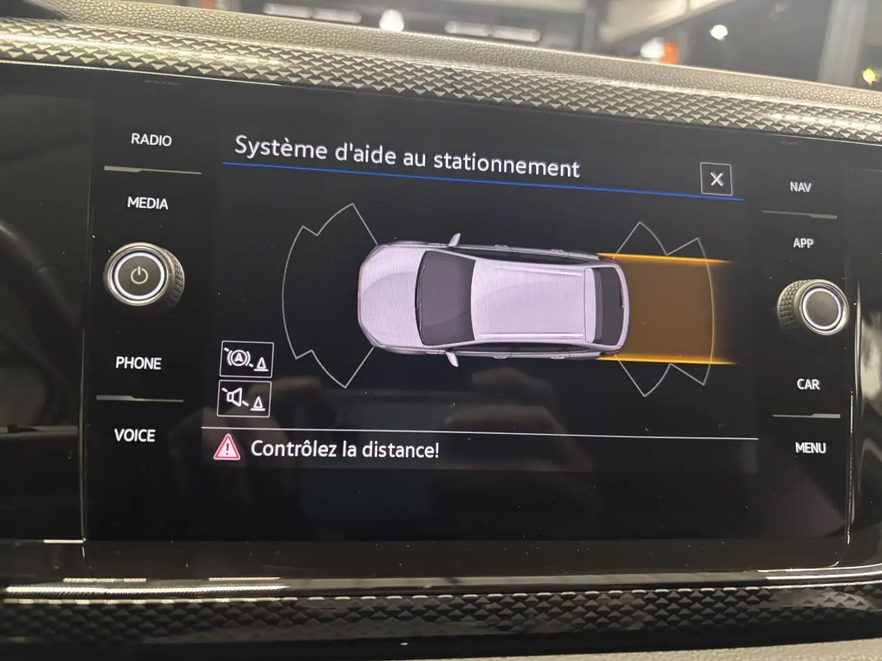Écran tactile intérieur du Volkswagen Taigo blanc montrant le système d'aide au stationnement vue de dessus du véhicule.