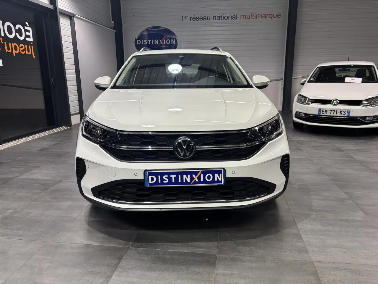Vue de face du Volkswagen Taigo blanc avec calandre noire et logo VW central dans un showroom.
