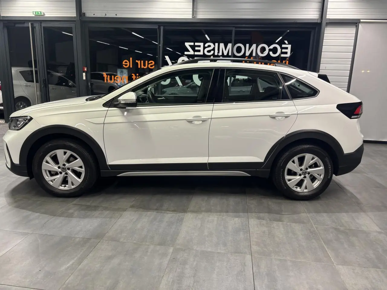 Vue latérale droite d’un Volkswagen Taigo blanc 2023 avec jantes alliage et protections noires sur les passages de roues.